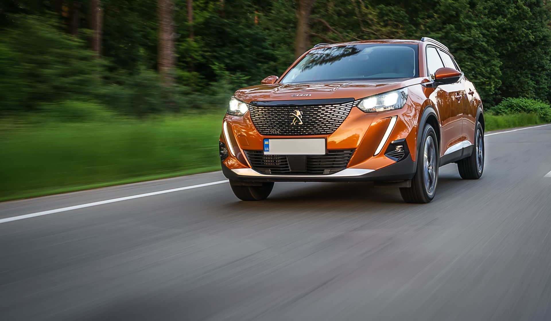 Un SUV orange roule sur une route asphaltée ; des arbres verts bordent la route.