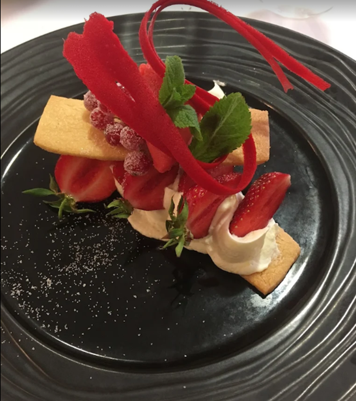 Dessert sur une assiette noire : fraises, crème, biscuits, rubans rouges, groseilles rouges, brins de menthe.