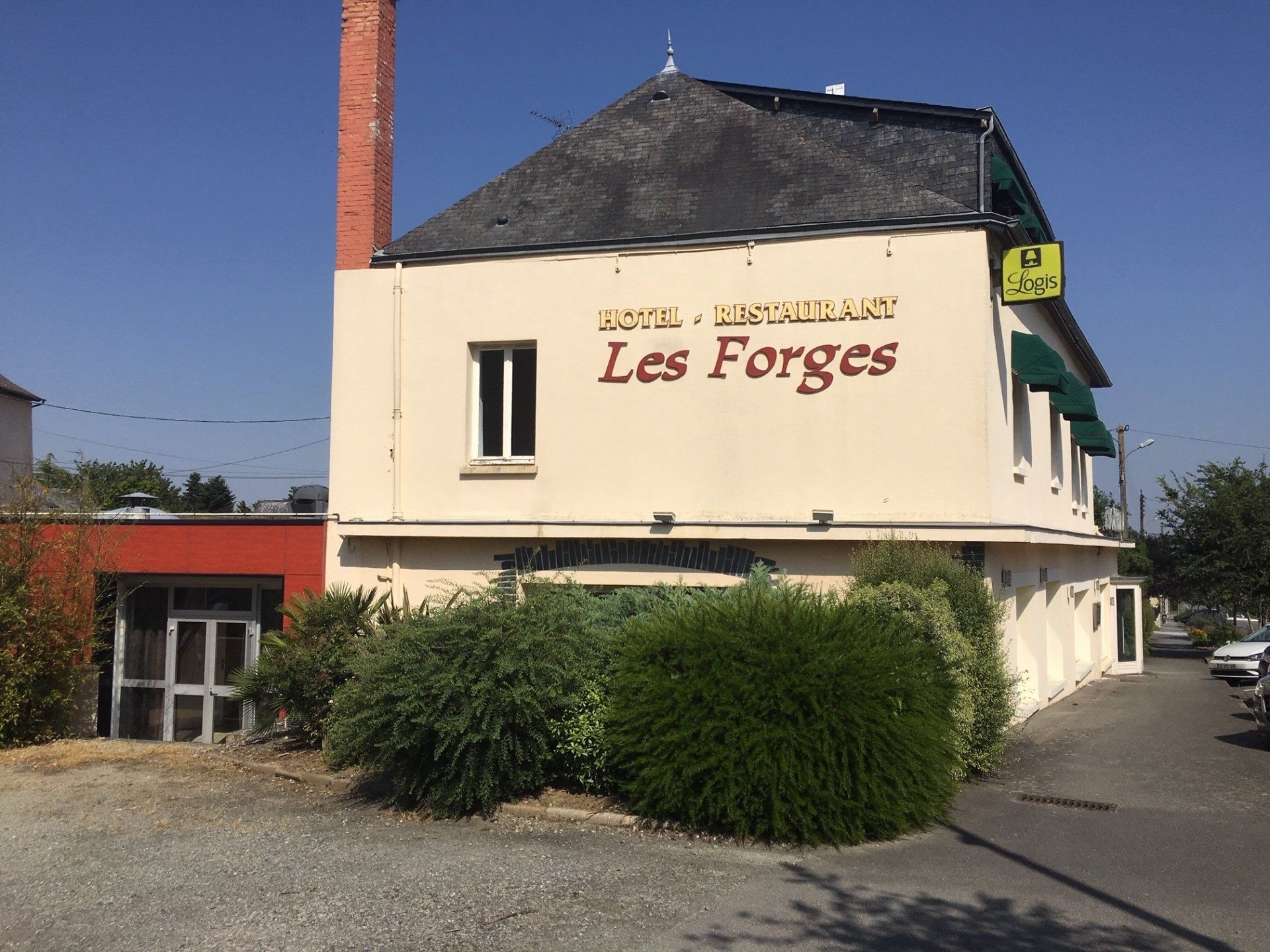 Bâtiment de l'hôtel-restaurant « Les Forges » avec cheminée en briques et panneau de parking.