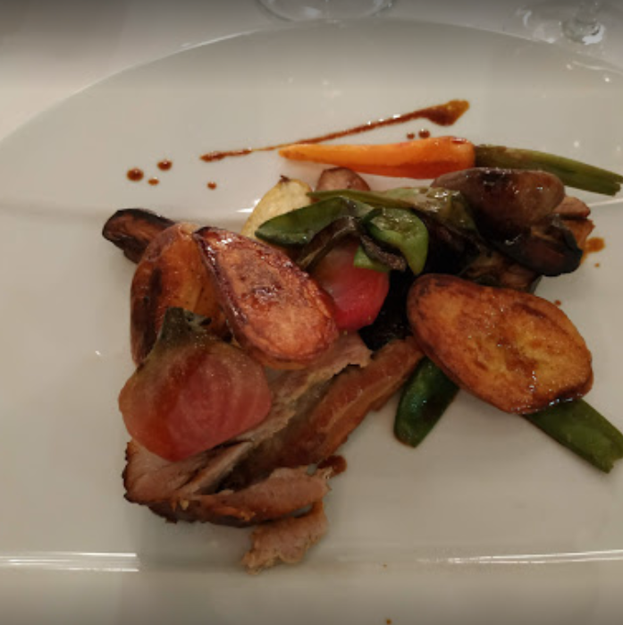 Viandes et légumes rôtis sur une assiette blanche, comprenant des carottes, des pommes de terre et des haricots, arrosés d'un filet de sauce.
