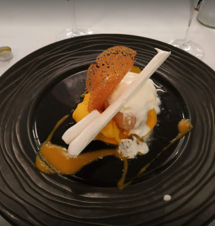 Dessert sur assiette noire : purée de mangue, glace, bâtonnets de meringue, biscuit dentelle et sauce.