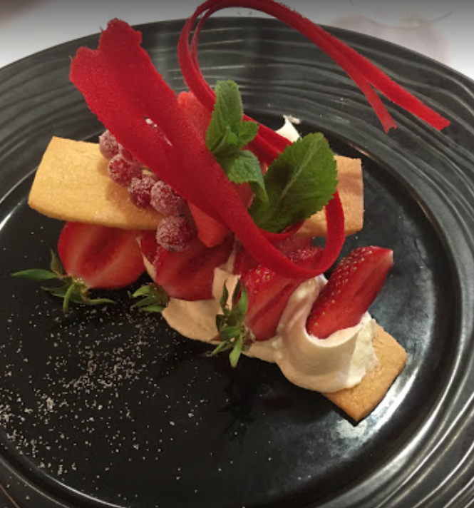 Dessert aux fraises servi sur une assiette noire, garni de rhubarbe rouge et de menthe.