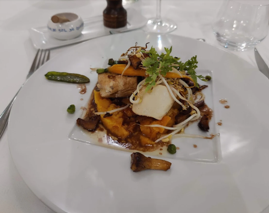 Plat gastronomique composé d'une protéine sur une purée de patates douces, garni de légumes et de germes, présenté dans une assiette carrée.