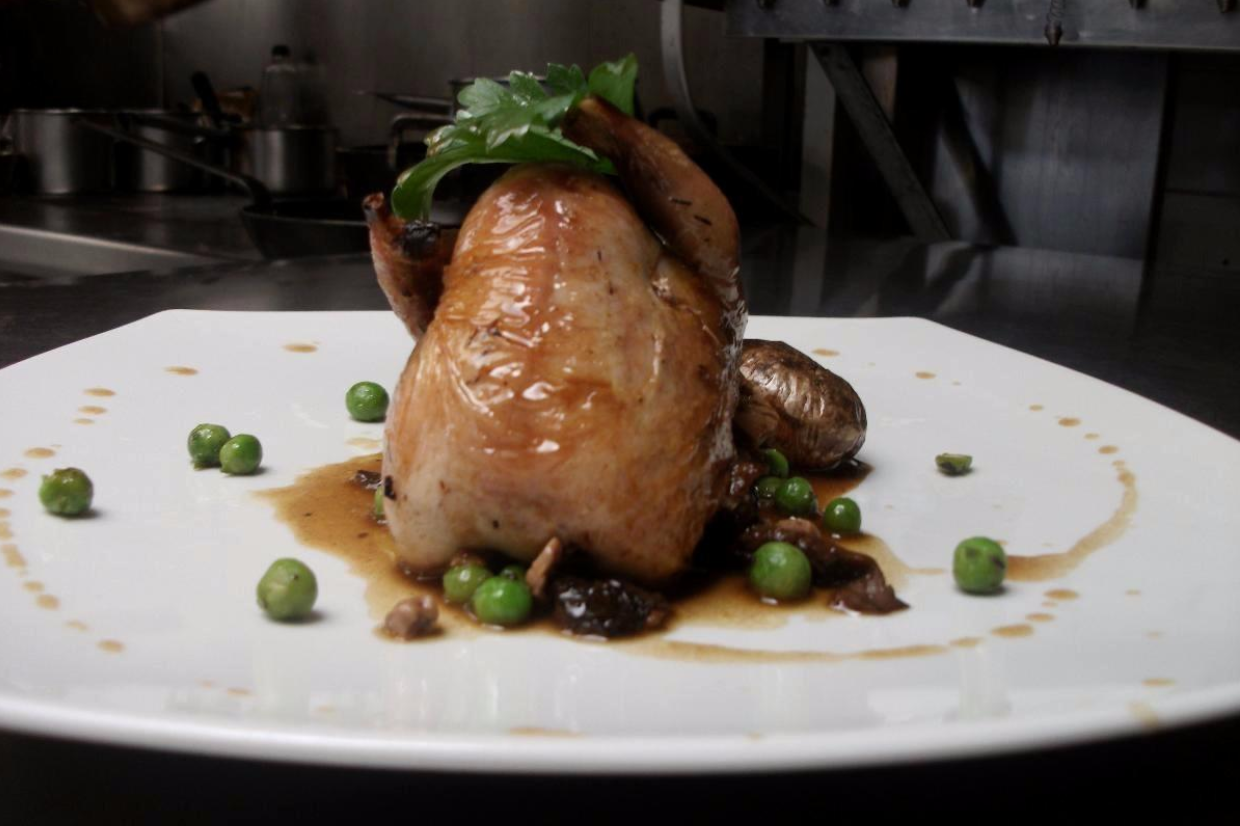 Caille rôtie sur assiette blanche avec petits pois, champignons et sauce.