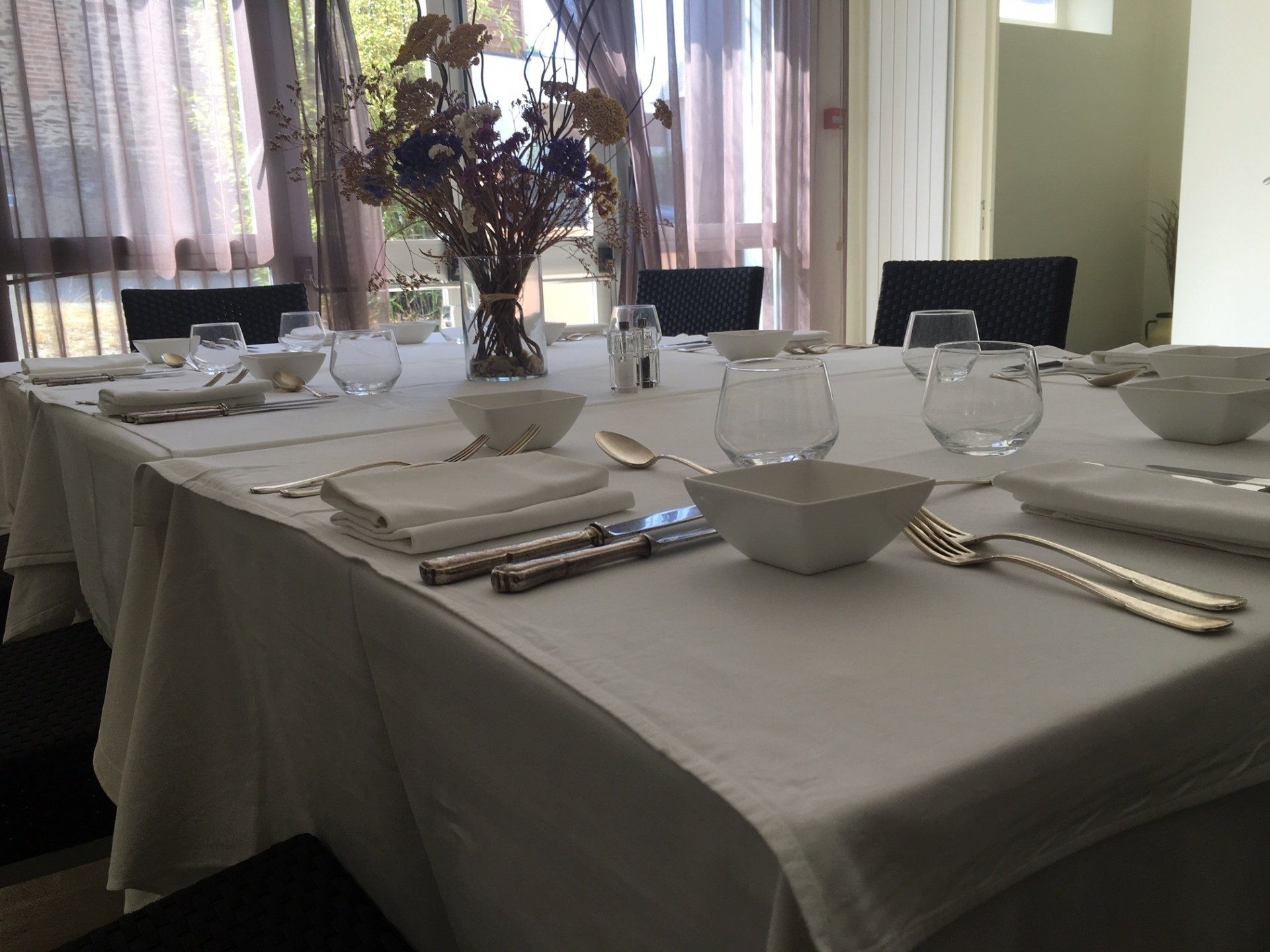 Une longue nappe blanche dressée pour un repas formel, avec couverts, verres et un centre de table floral.