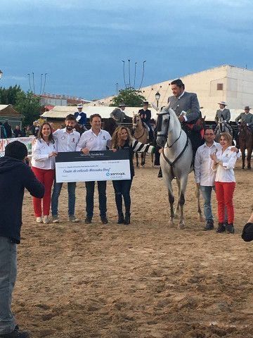 Personas posando con un jinete en un caballo blanco en un evento al aire libre, sosteniendo una pancarta.