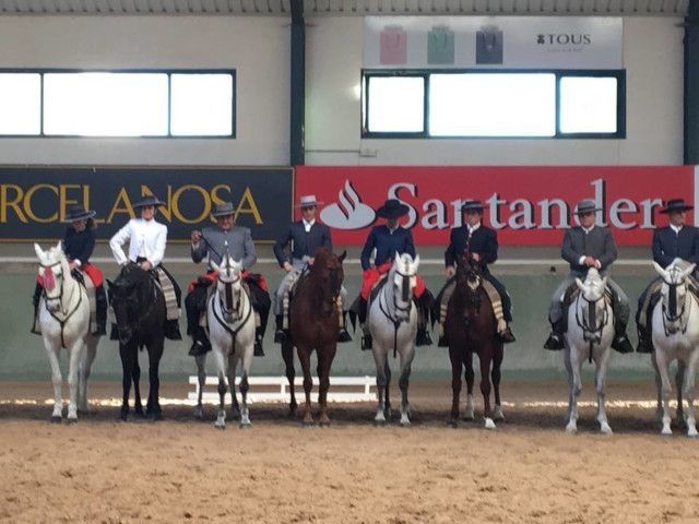 Fila de jinetes a caballo en una pista cubierta con pancartas de patrocinadores detrás.