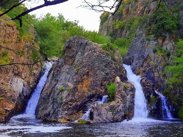Arroyo de montaña que cae en cascada sobre rocas en un cañón verde con dos cascadas.