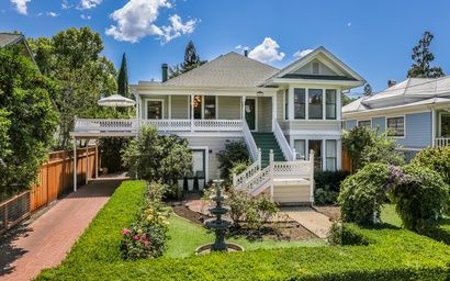 Outside view of Casa Rosa House rental in St. Helena, a large white house with a green porch is surrounded by trees and bushes .