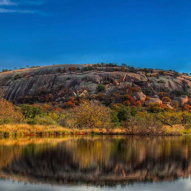 Enchanted Rock with trees reflected in the water .