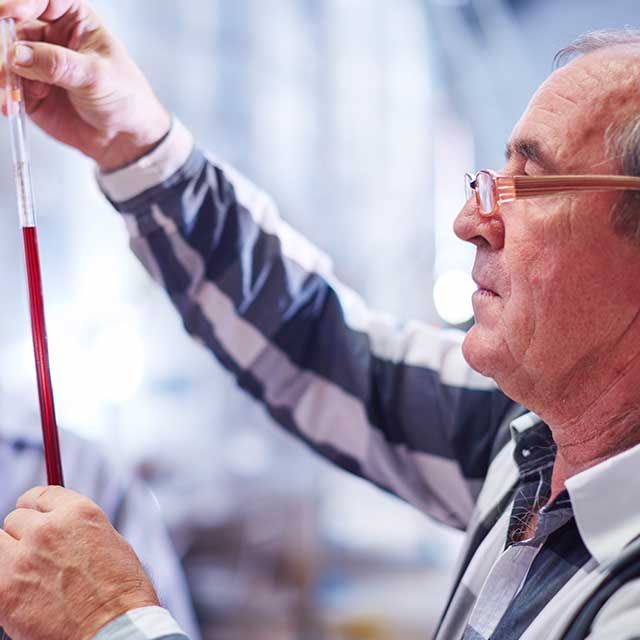 a man is holding a test tube with a red liquid in it