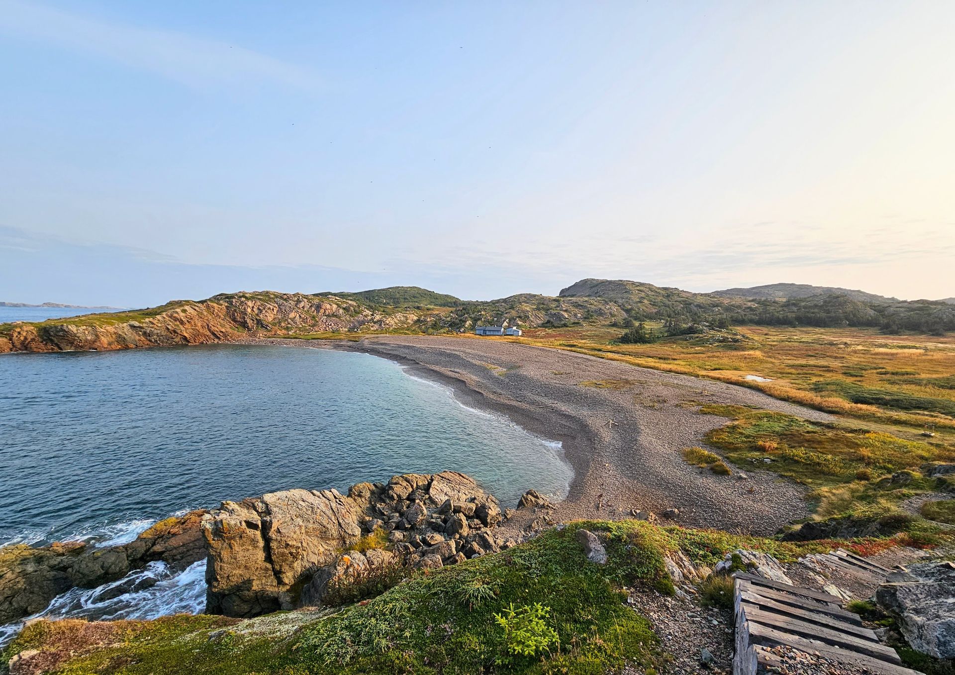 A wooden walkway leading to a rocky beach next to a body of water.