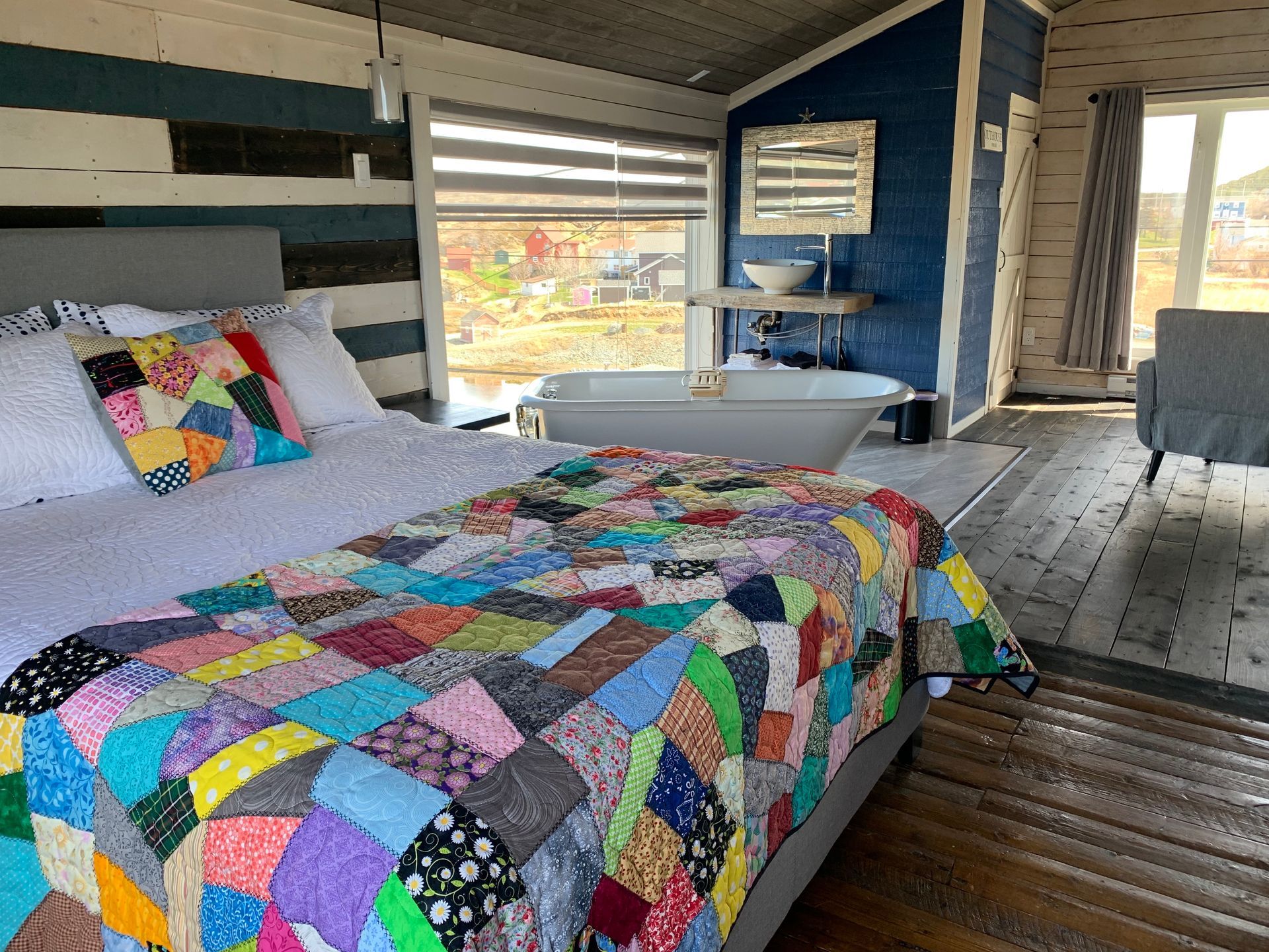 A bedroom with a colorful quilt and a bathtub.