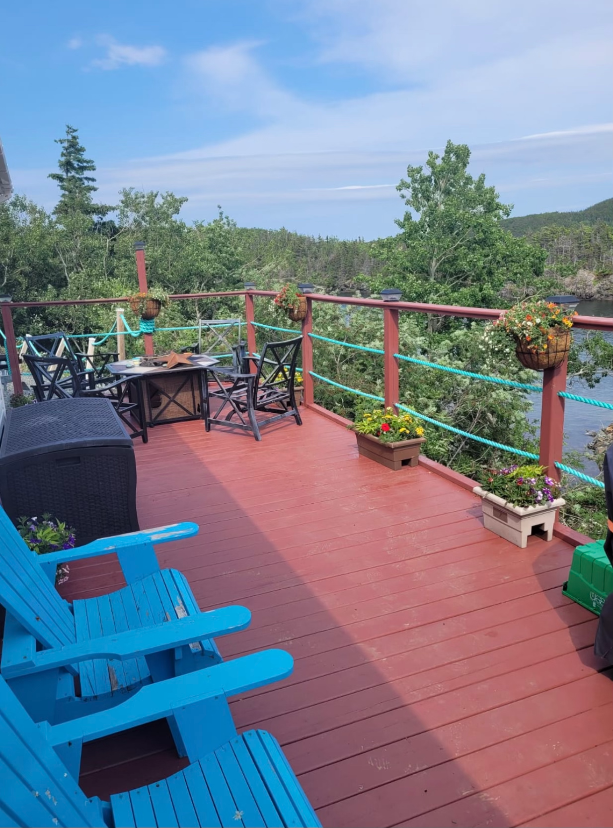 A deck with blue chairs and a table and chairs overlooking body of water