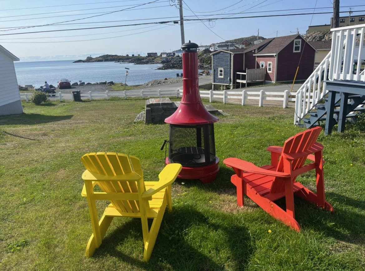 Three lawn chairs are sitting in the grass next to a fire pit.