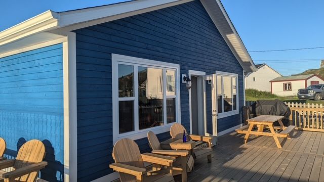 A wooden deck with chairs and a railing overlooking a body of water
