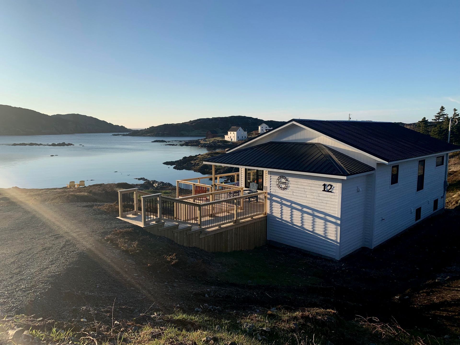 A white house with a large deck overlooking a body of water.