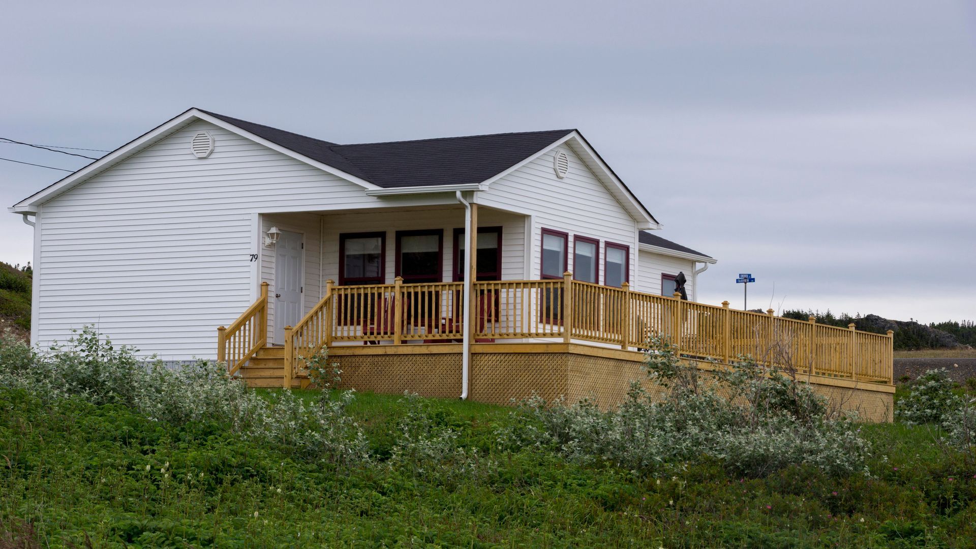 A white house with a wooden deck is sitting on top of a grassy hill.