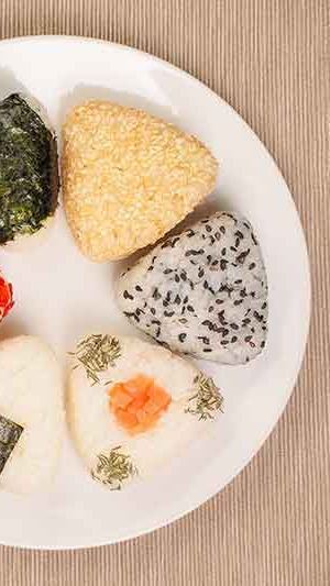 Teller mit japanischen Onigiri (Reisbällchen) mit verschiedenen Toppings und Sesamsamen.