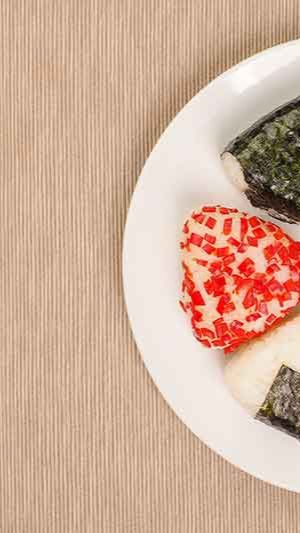 Teller mit drei dreieckigen Onigiri, eines mit rotem Belag, eines mit Algenhülle.