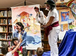 Un grupo de personas está realizando un espectáculo de marionetas en una biblioteca.