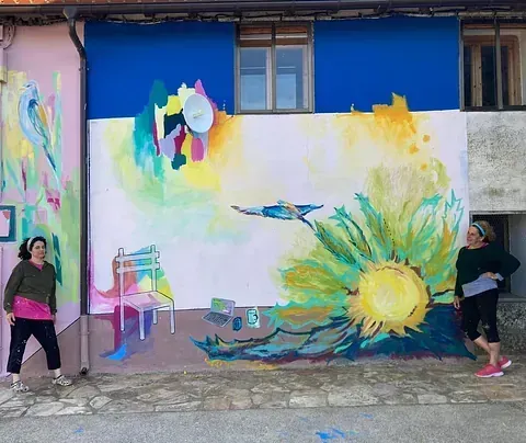 Dos mujeres están paradas frente a un gran mural en el costado de un edificio.