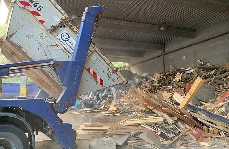 Ein Muldenkipper kippt Holz auf einen Holzstapel