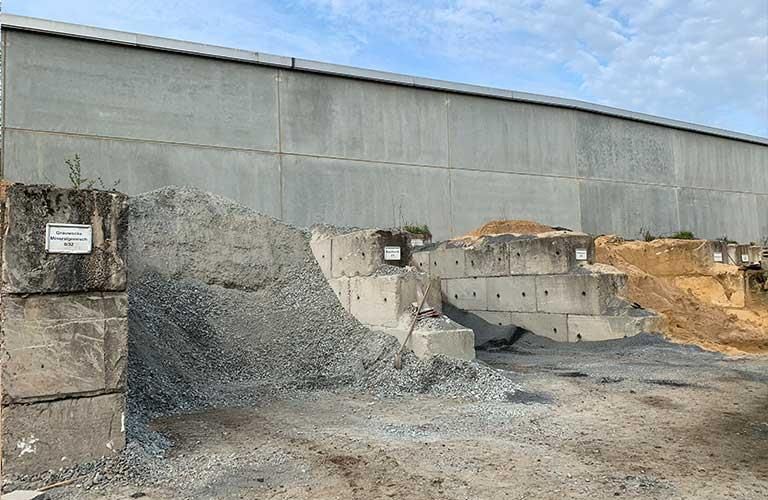 Vor einer Betonmauer steht ein Kieshaufen.