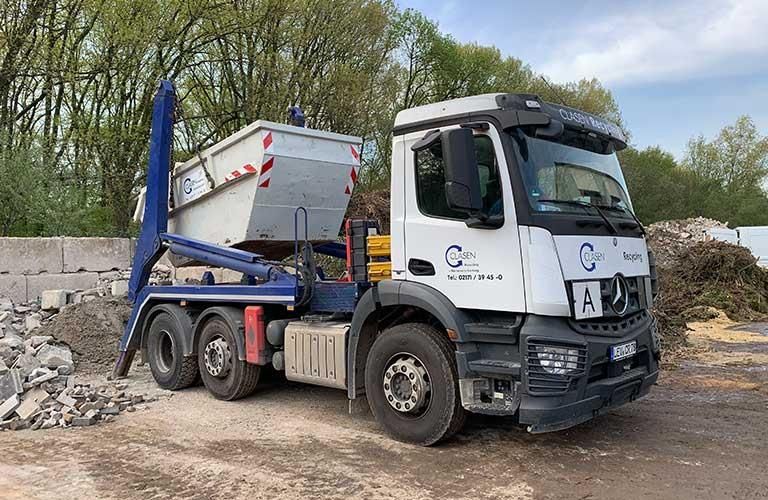 Ein Muldenkipper ist auf einem unbefestigten Parkplatz neben einem Steinhaufen geparkt.
