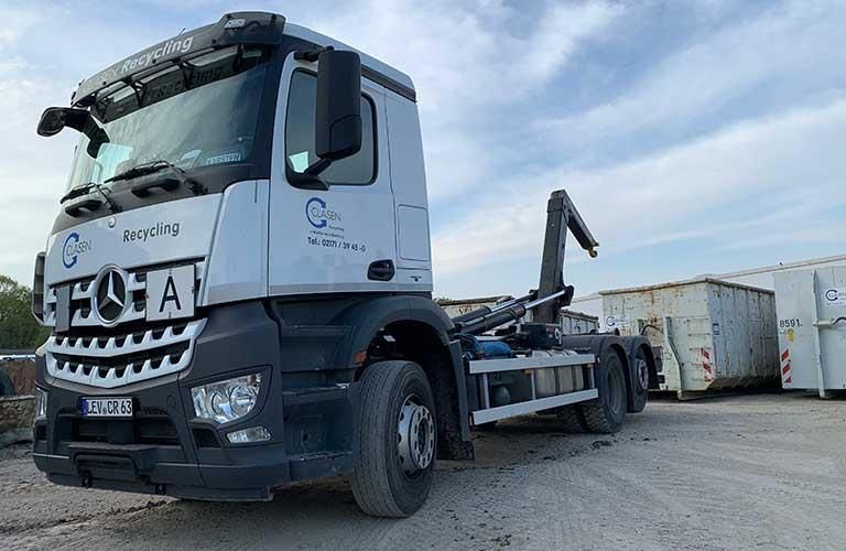 Ein weißer Lastwagen steht auf einem Schotterplatz neben einem Müllcontainer.