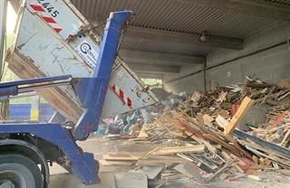 Ein Muldenkipper lädt Holz auf einen Holzstapel.