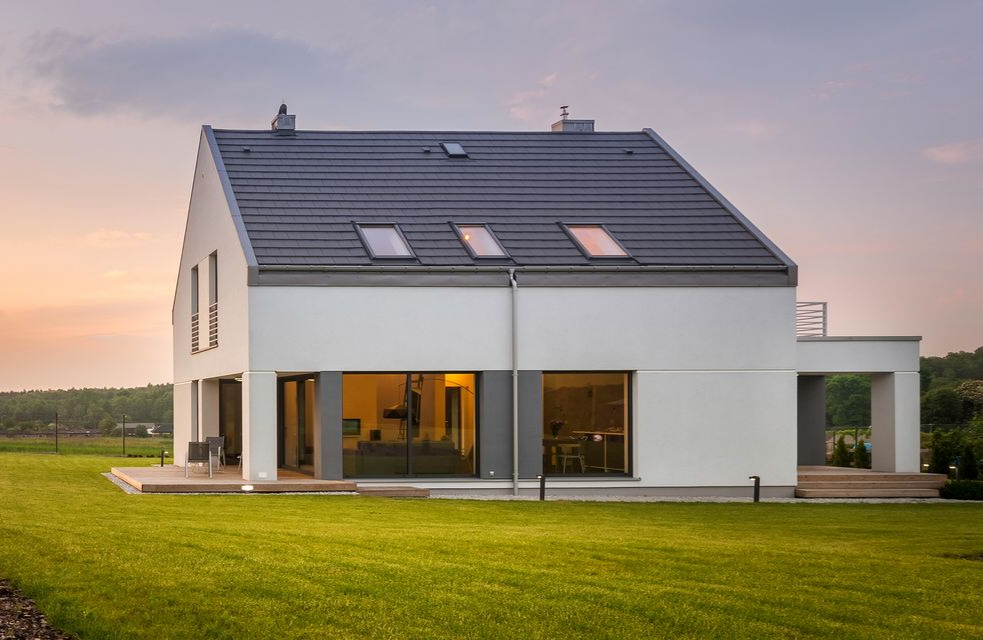Maison moderne blanche de deux étages avec un toit gris, de grandes fenêtres et une pelouse verte.