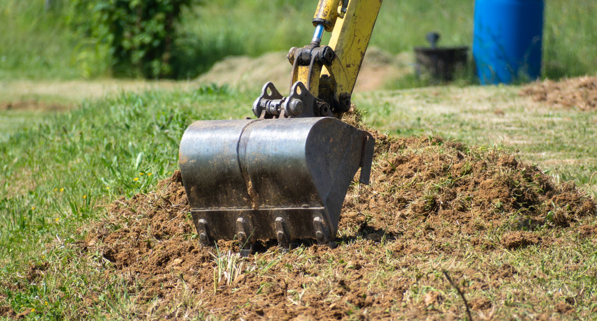 Le godet d'une excavatrice ramasse de la terre et de l'herbe dans un champ verdoyant.