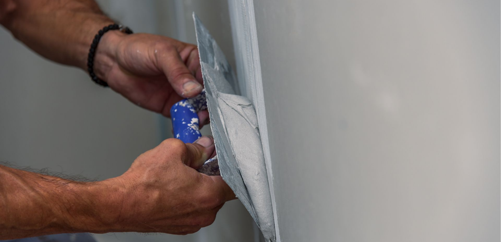 Des mains tenant un couteau à plâtre, appliquant de l'enduit sur un mur.