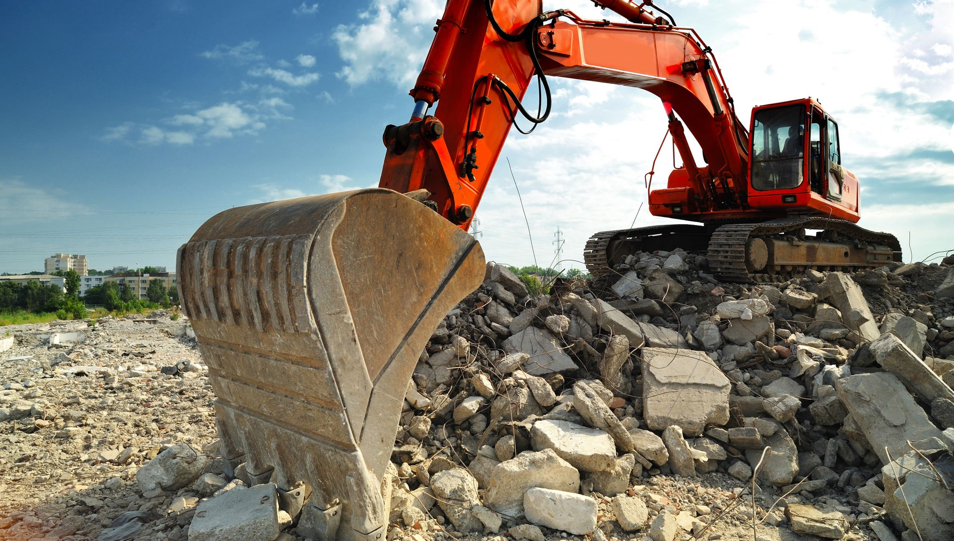 Godet d'excavatrice orange ramassant des gravats sur fond de ciel bleu.