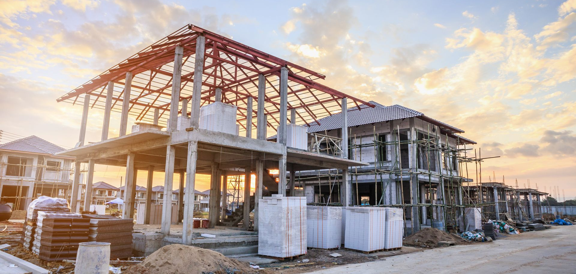 Bâtiments en construction avec charpente apparente au coucher du soleil.