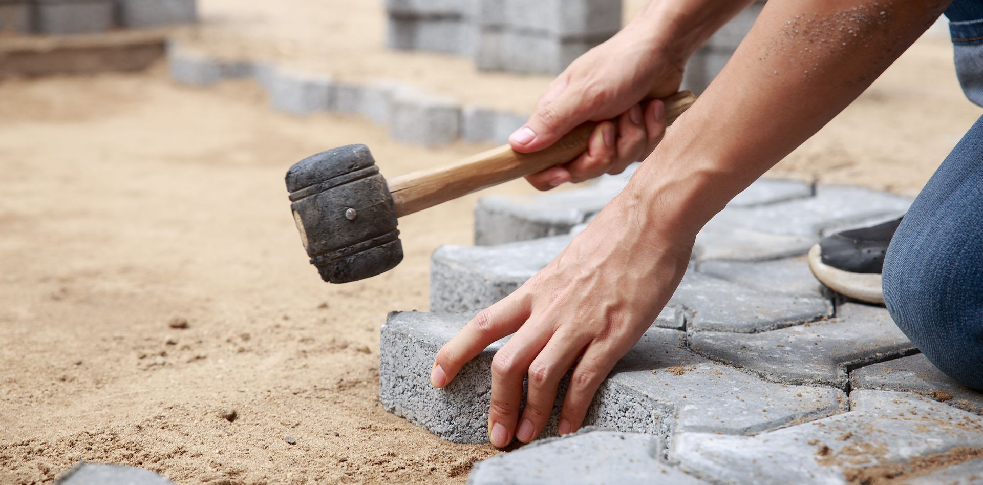 Personne utilisant un maillet pour installer des pavés autobloquants.