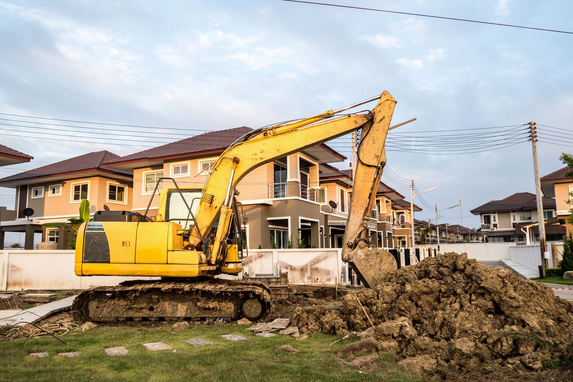 Une pelleteuse jaune creuse devant des maisons neuves, sous un ciel nuageux.