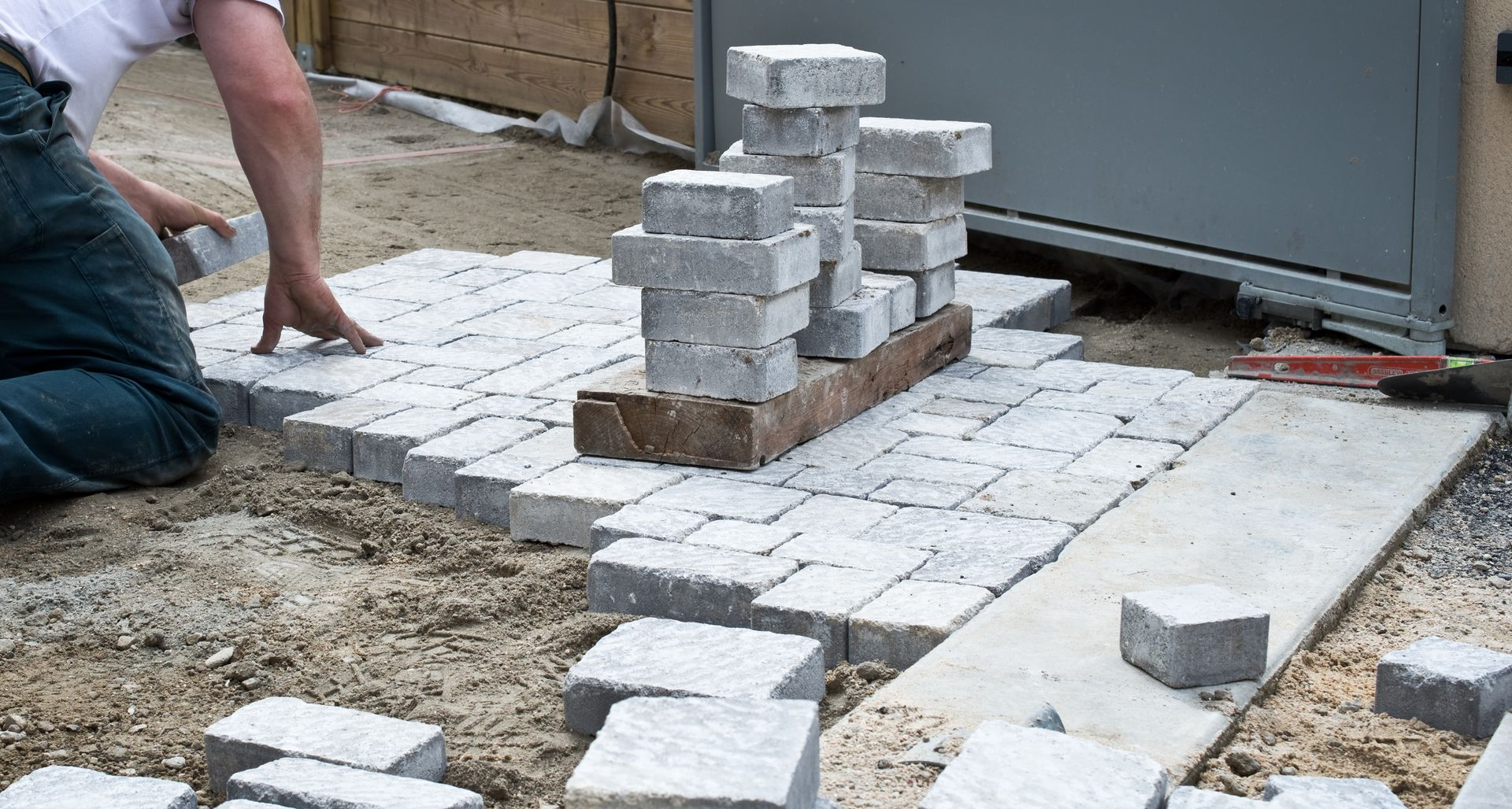 Une personne pose des pavés gris à l'extérieur.