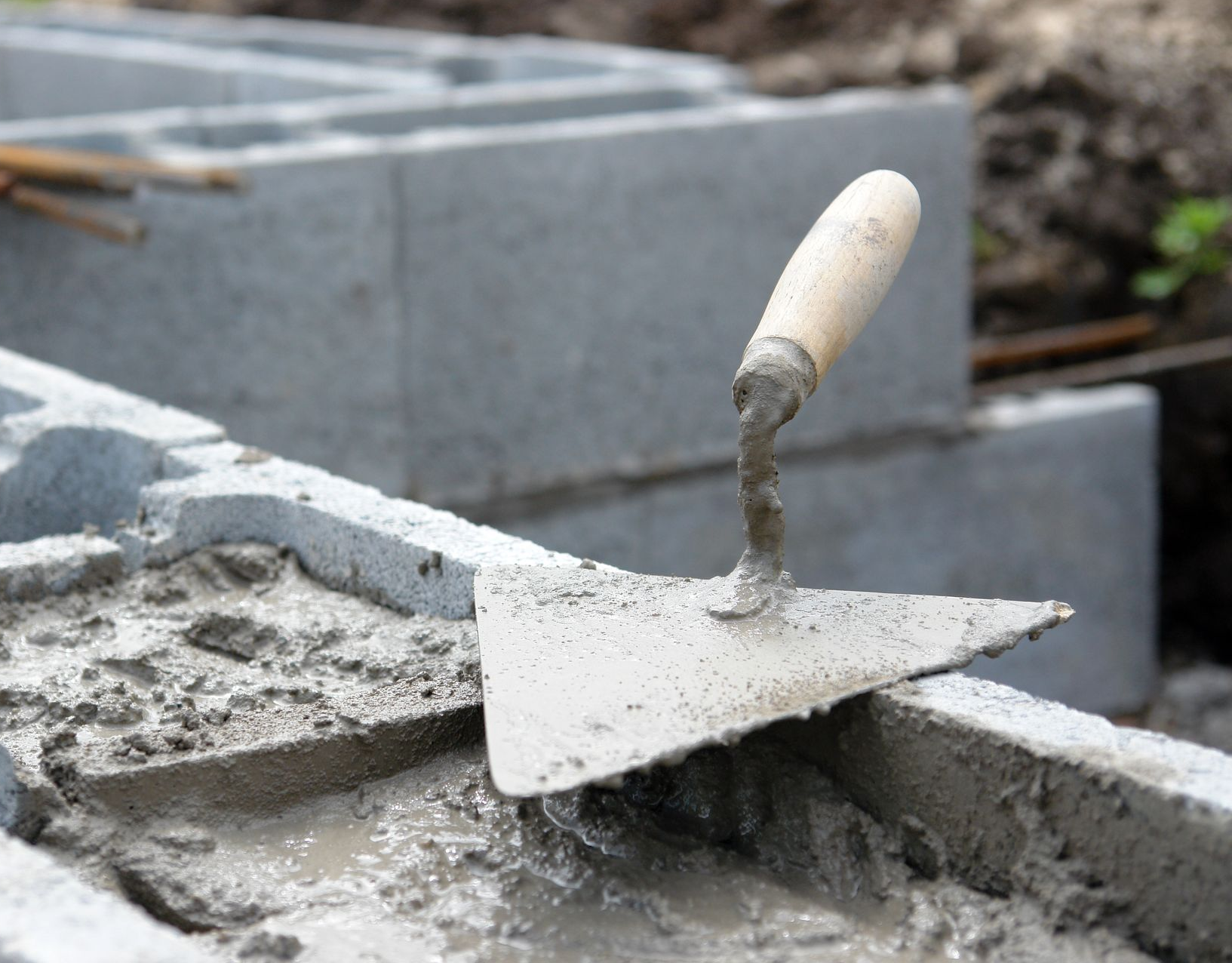 Truelle enduite de ciment frais sur un parpaing, à côté de blocs empilés ; chantier de construction.