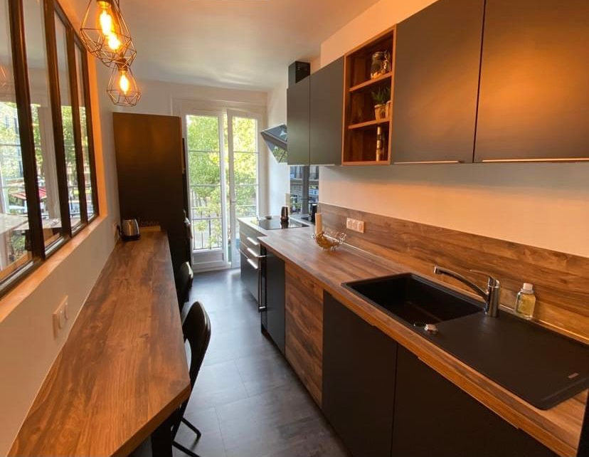 Cuisine moderne avec des armoires foncées, des comptoirs en bois et une longue table à manger.