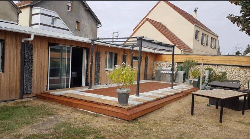 Terrasse en bois avec pergola, donnant sur un jardin avec une table à manger et des plantes en pot.