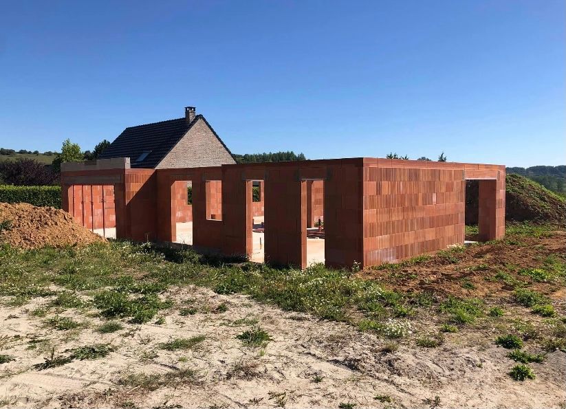 Chantier : murs en briques rouges d'une maison en construction ; ciel bleu, terre et verdure.