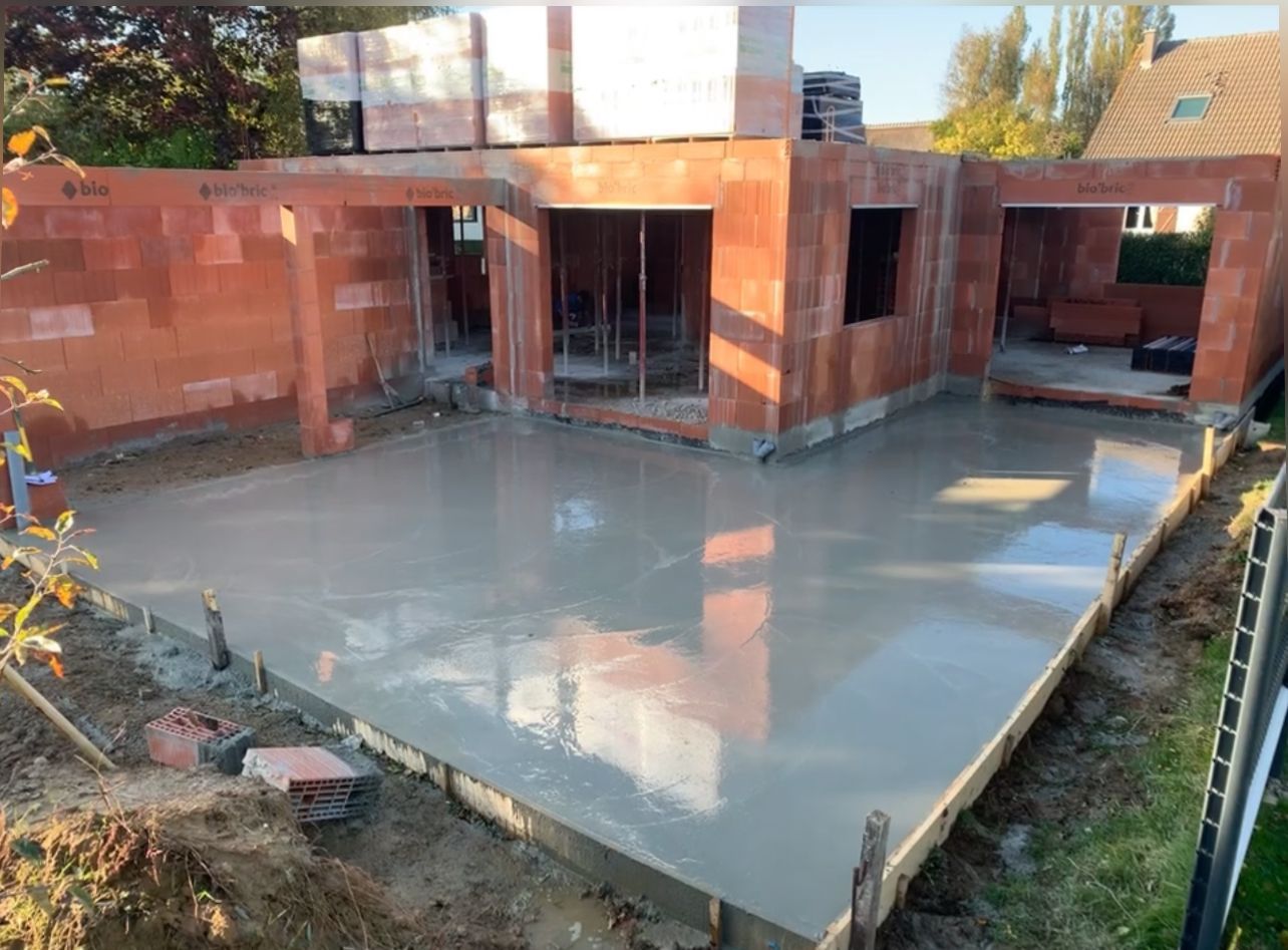 Chantier de construction avec fondations en béton et murs de briques, baigné de lumière naturelle.