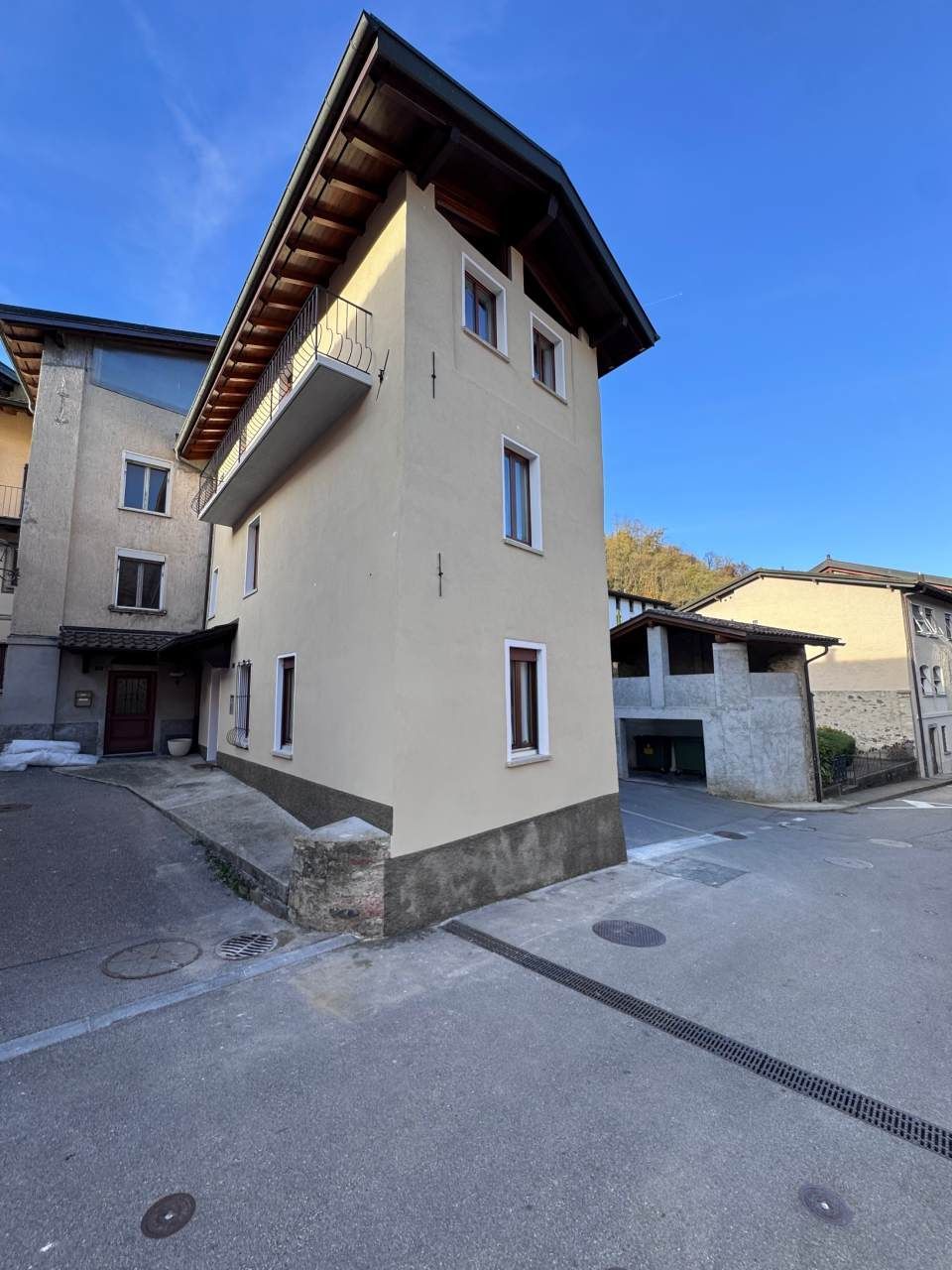 Un alto edificio color crema con un balcone si erge all'angolo di una strada, un altro edificio lì vicino e il cielo è terso.