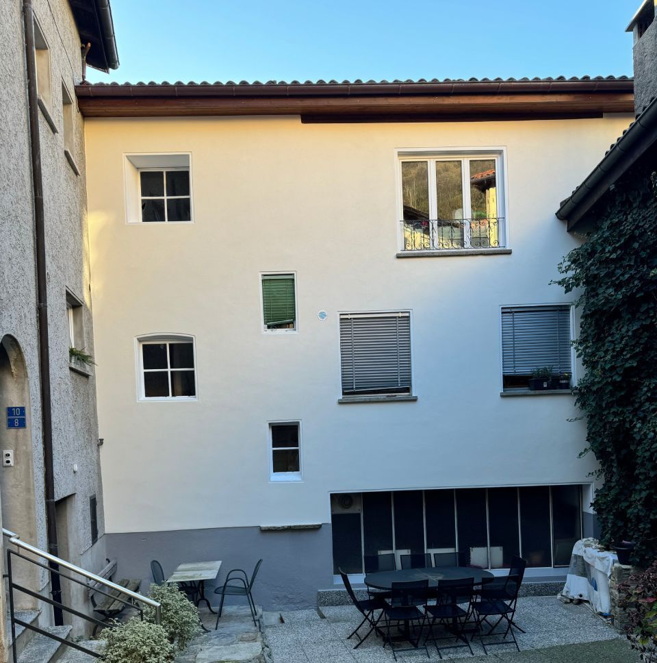 Esterno di un edificio bianco con finestre di varie dimensioni, area salotto all'aperto ed edera.