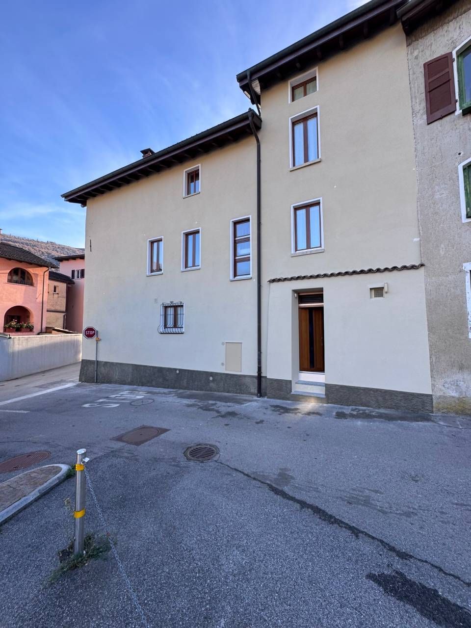 Facciata di un edificio su una strada, stucco beige, numerose finestre, porta marrone, cielo coperto.