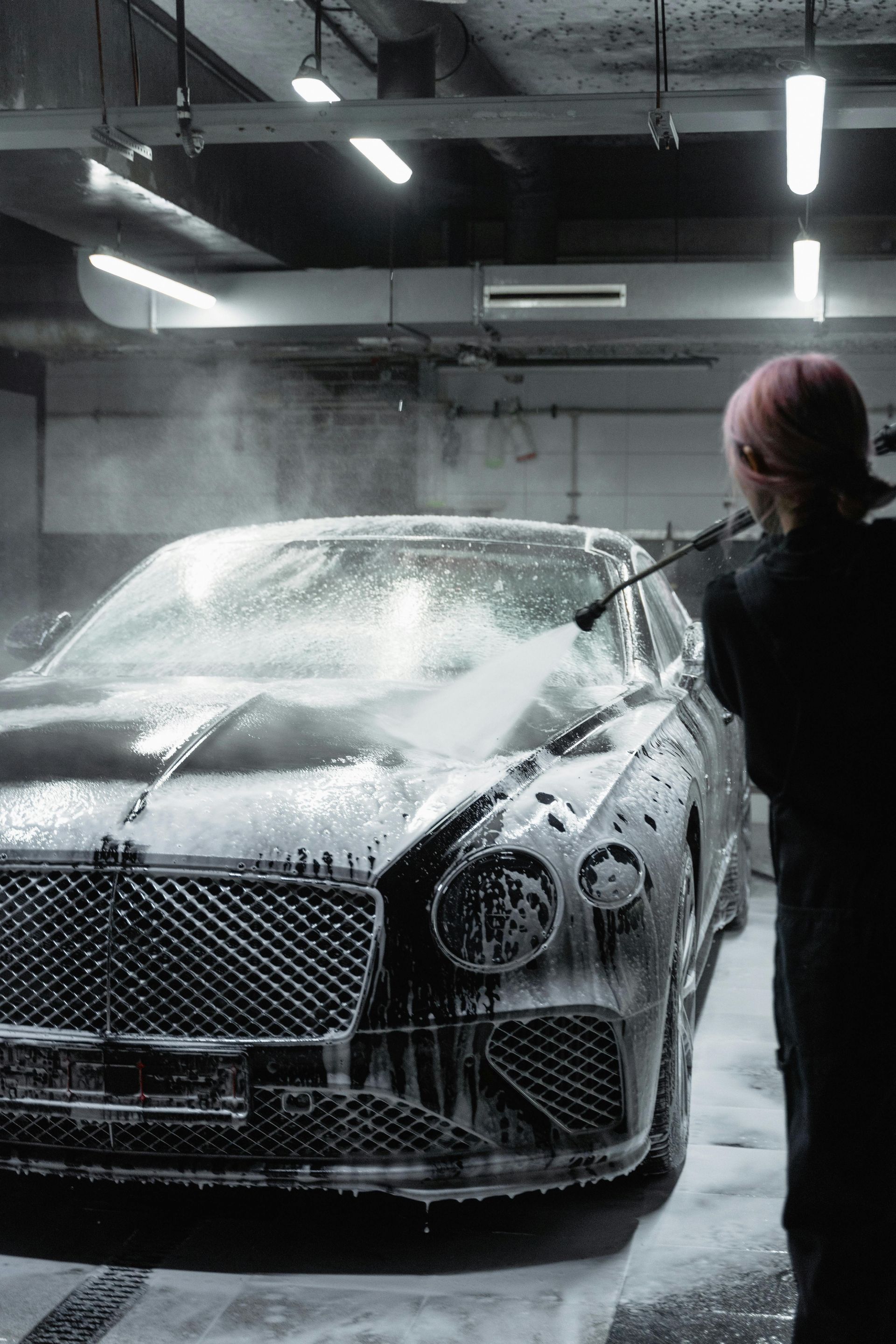 Persona lavando un Bentley negro con una manguera de alta presión en un lavadero de automóviles.