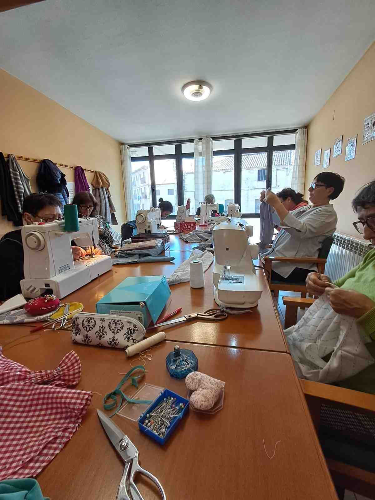 Varias personas están sentadas alrededor de una mesa larga en una habitación luminosa, utilizando máquinas de coser 