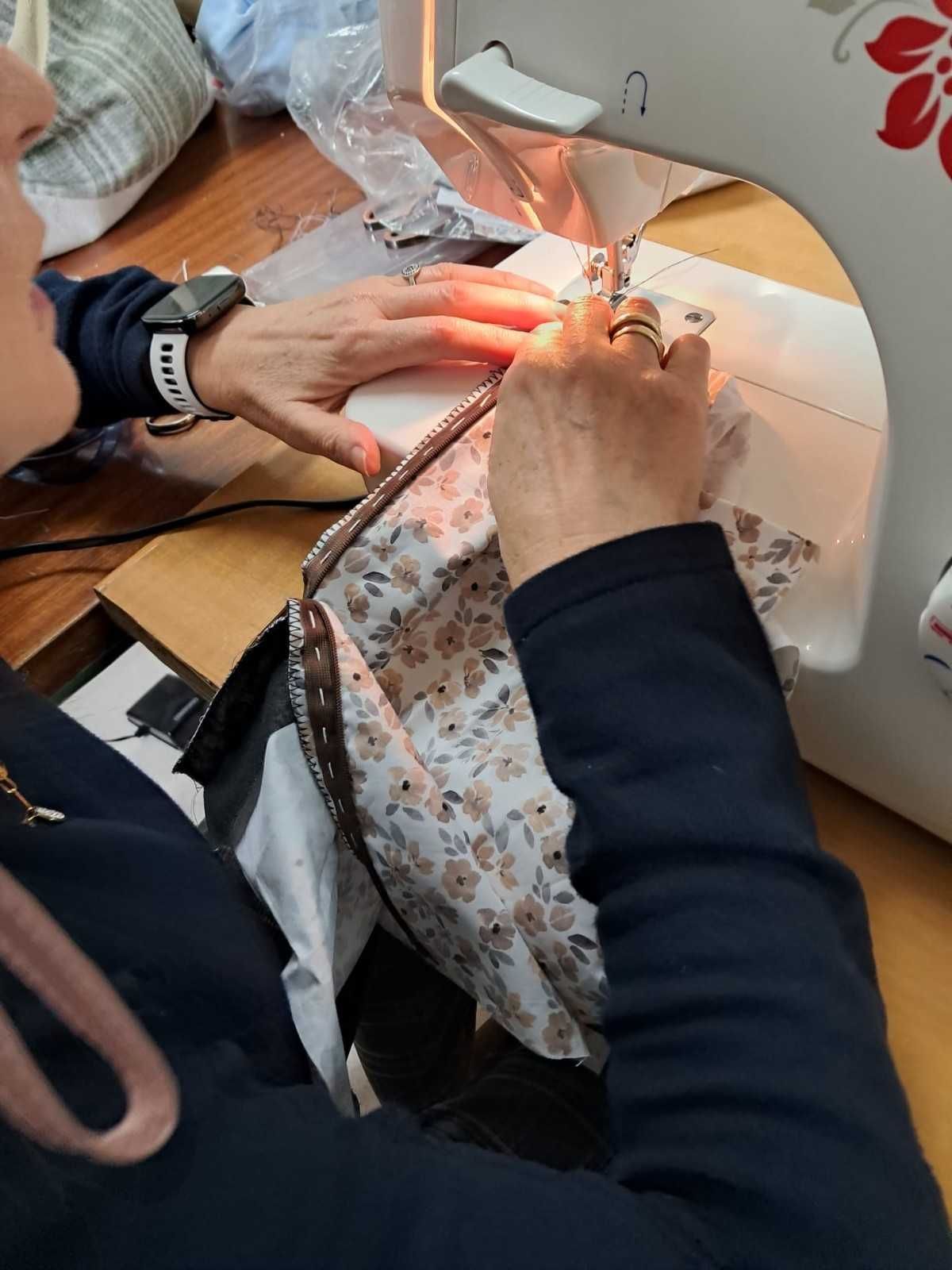 Una persona cose tela con estampado floral con una máquina de coser blanca sobre una mesa de madera.